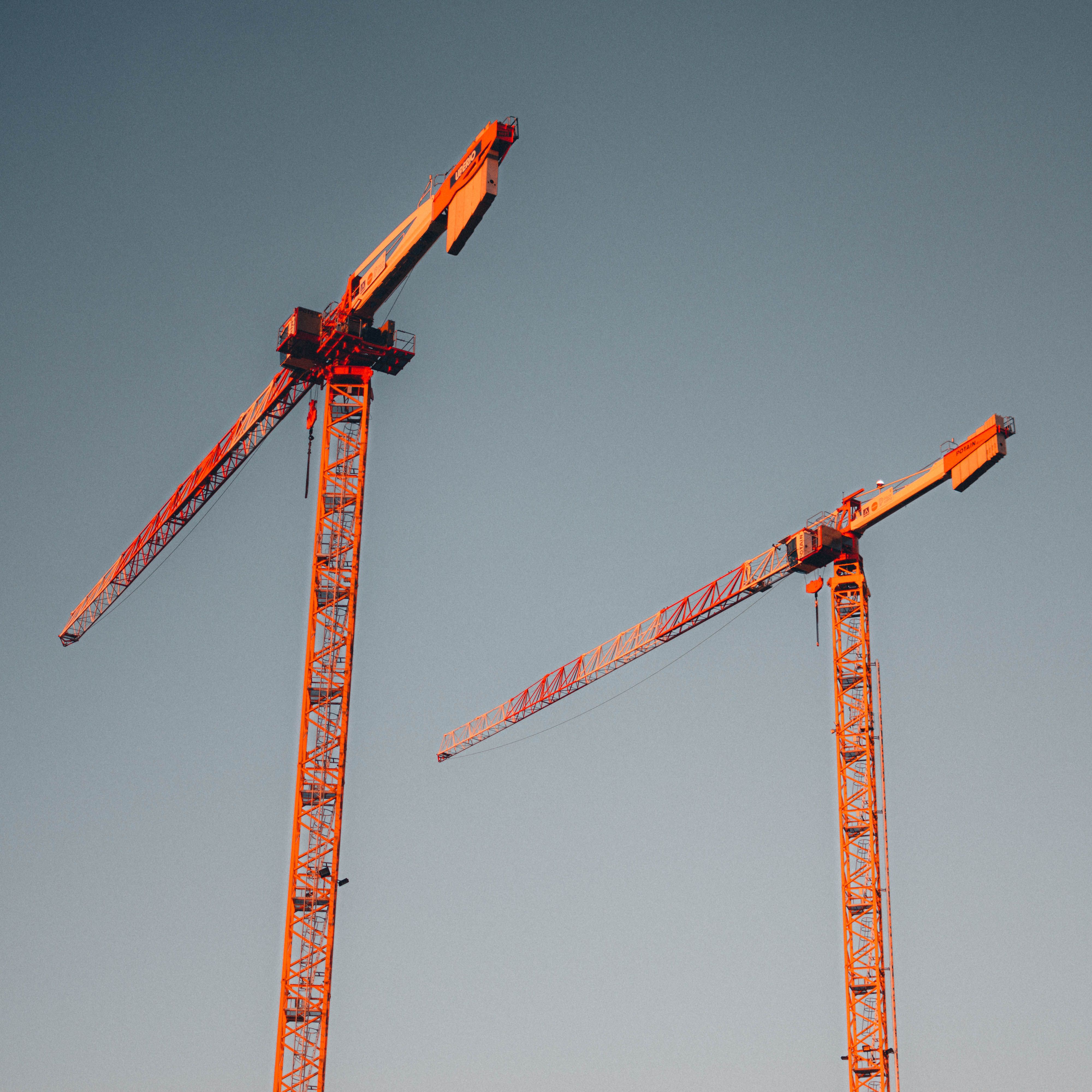 Two red tower cranes stand tall against a clear sky, symbolizing urban development.