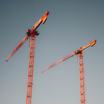 Two red tower cranes stand tall against a clear sky, symbolizing urban development.