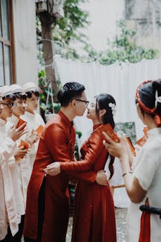 A couple in traditional attire celebrates their wedding with friends cheering.