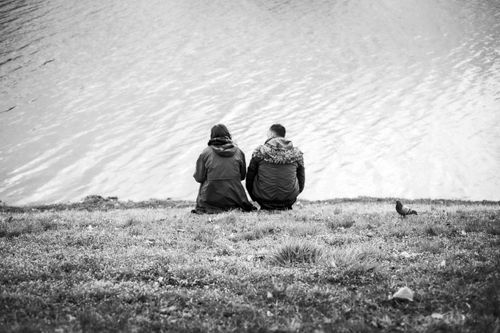 Free A couple in warm coats sitting by a serene lake, depicting a moment of tranquility. Stock Photo