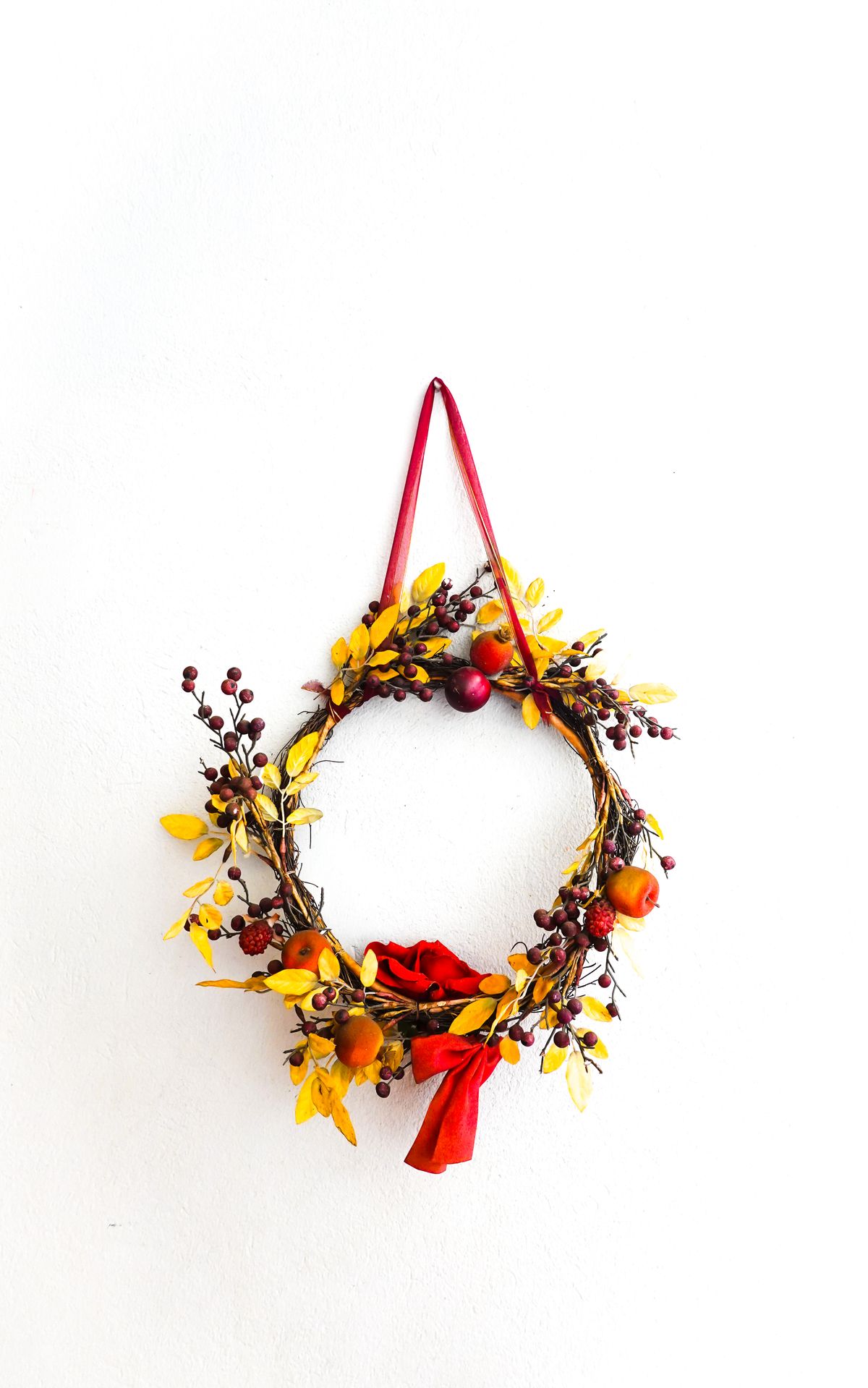 Colorful autumn wreath with berries, yellow leaves and ribbon on a white wall