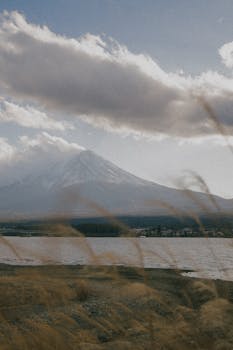 Mount Fuji towering amidst a cloudy sky with a serene body of water in the foreground.