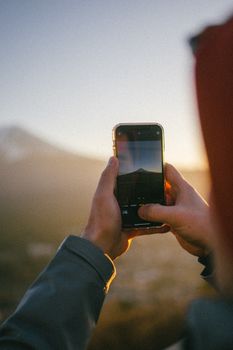 Hands holding a smartphone capturing a scenic mountain sunset view.