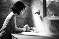 镜子里映出一张黑白图像，一名女子在老式浴室中倚靠着水槽