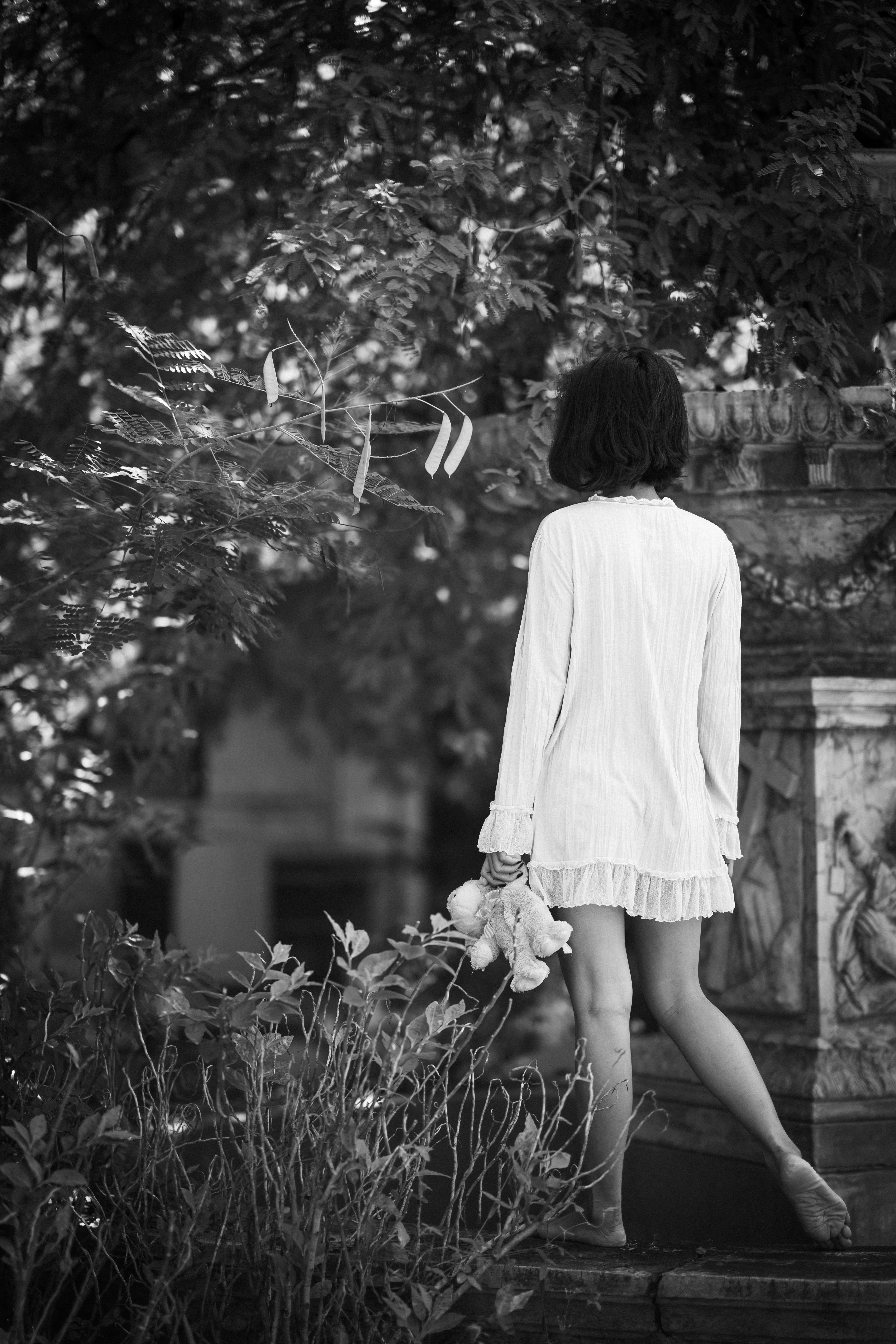 grey scale photography of barefooted woman holding a doll