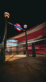 Nighttime view of London Underground entrance with moving double-decker bus.