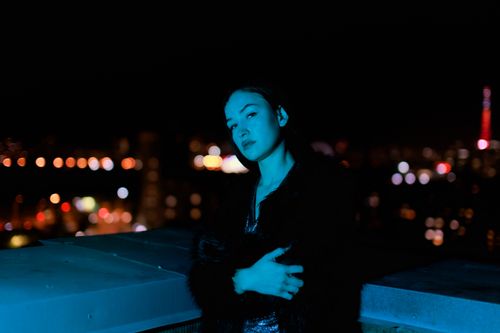 Free A woman poses on a rooftop with a city skyline in the background, bathed in blue light. Stock Photo