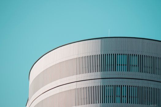 Striking modern cylindrical building with sleek design against a clear blue sky in Milan, Italy.