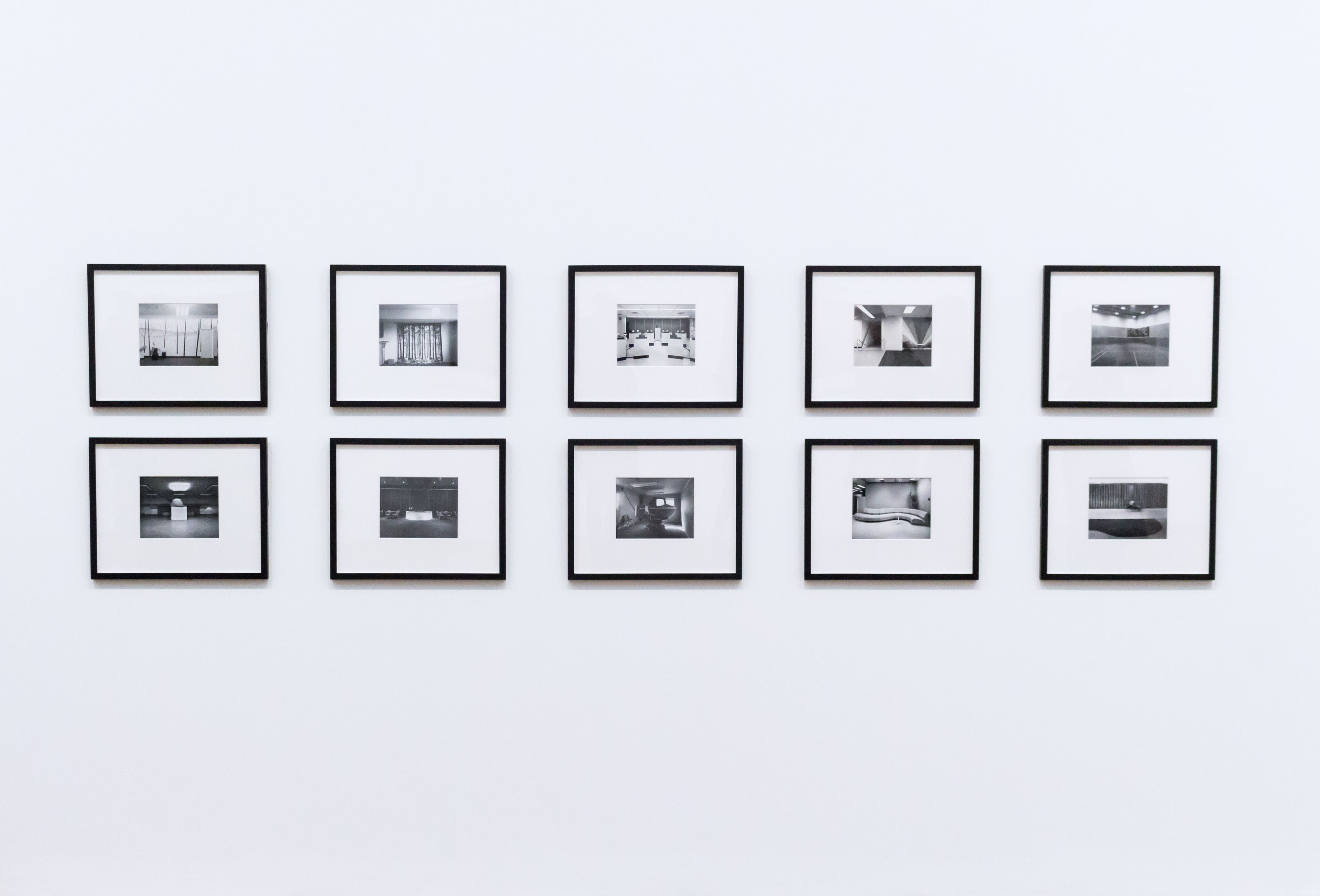 Ten small black-framed prints hung in two even rows on a white wall