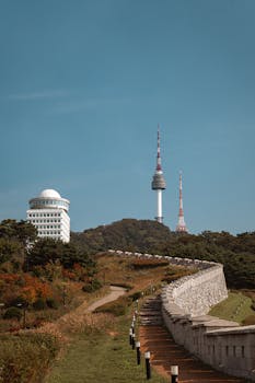 Namsan Tower in Seoul surrounded by lush greenery and historic walls during fall season.