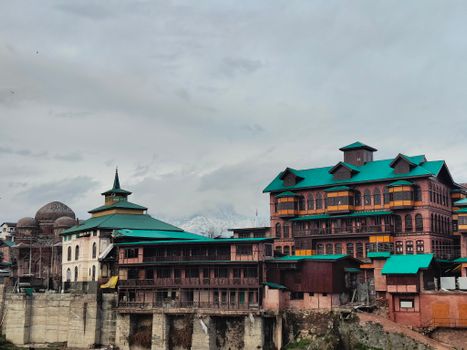 View of traditional architecture against snow-capped mountains under a cloudy sky.