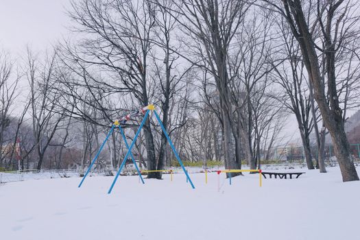 A serene winter scene of a quiet playground covered in snow, featuring a vibrant blue swing set.