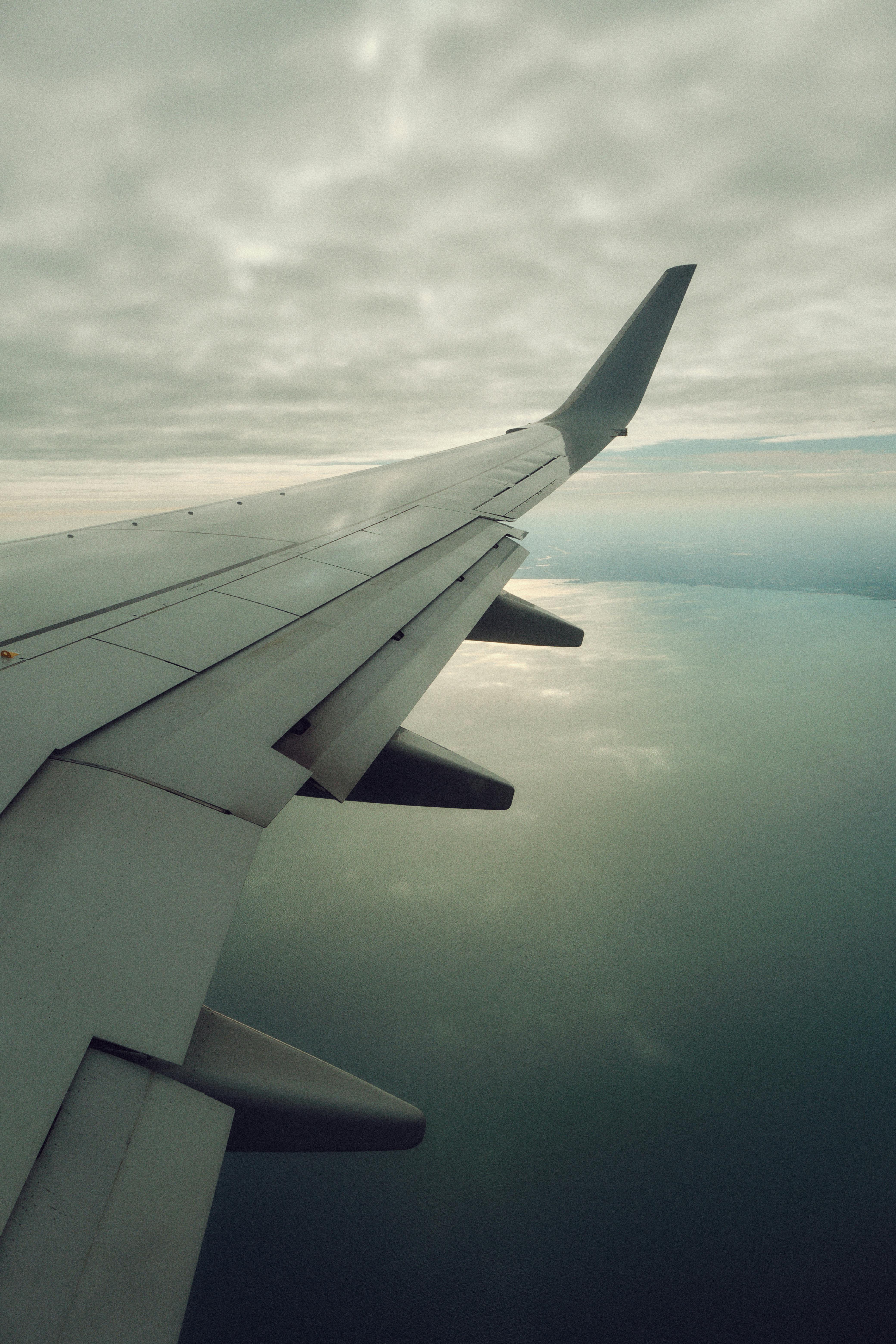 View from airplane window showing wing over a cloudy ocean, creating a serene aerial perspective.