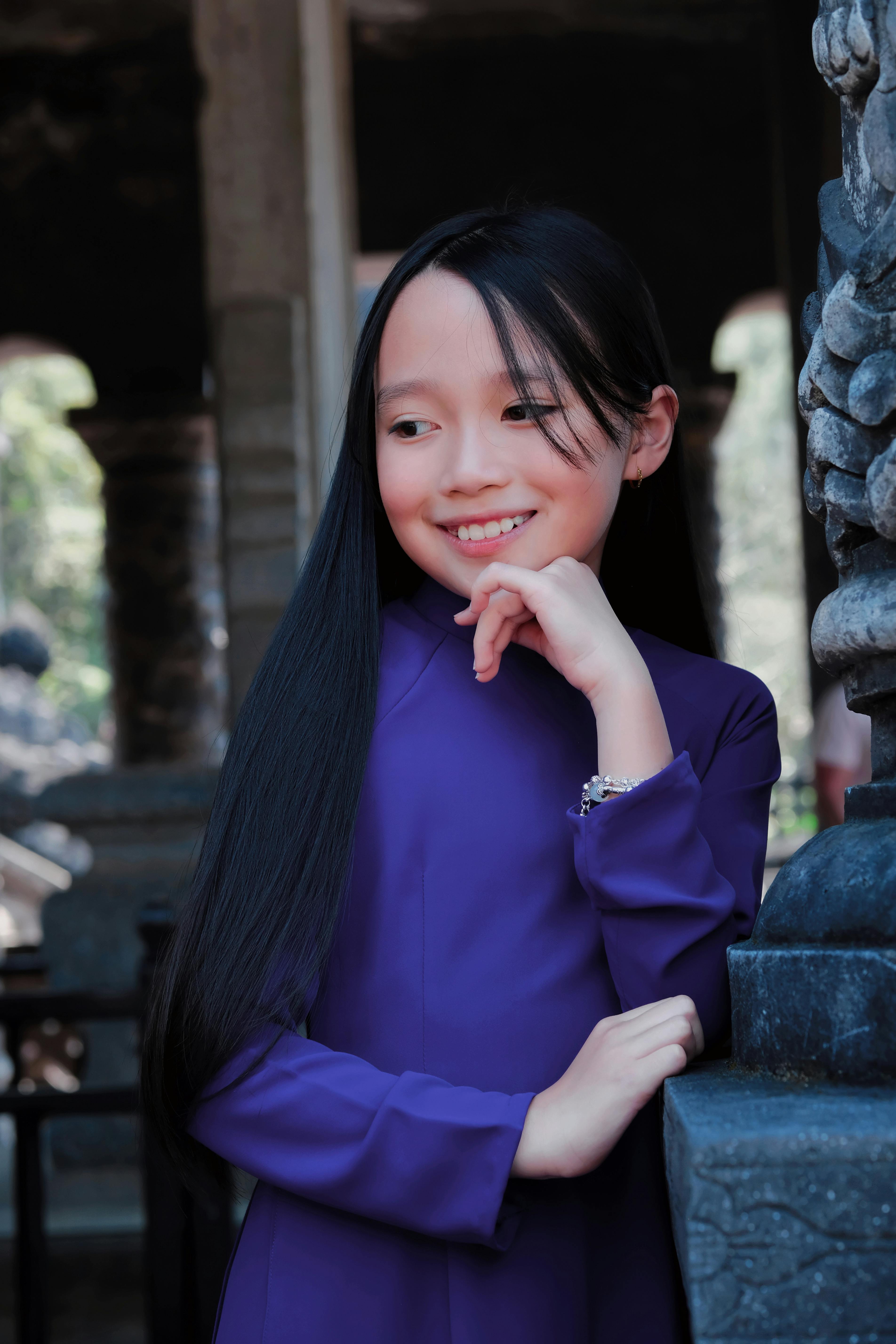 Smiling girl in purple Ao Dai at historic site in Hue, Vietnam.