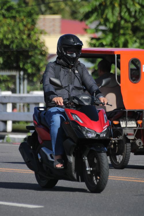 Free Rider wearing helmet and jacket on a red scooter in Tabaco City, Philippines. Stock Photo