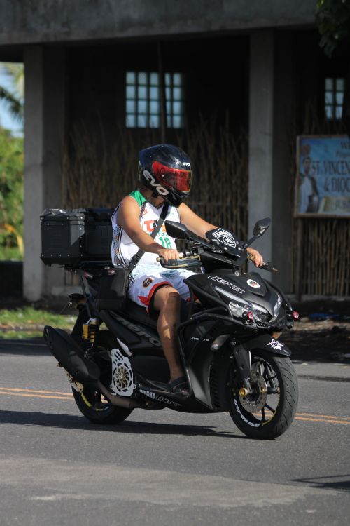 Free Adult motorcyclist riding a black scooter on a sunny urban road. Stock Photo