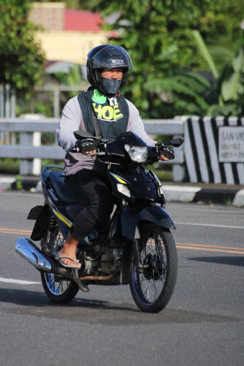 Free A motorcyclist drives along a city road, wearing a helmet and casual attire. Stock Photo