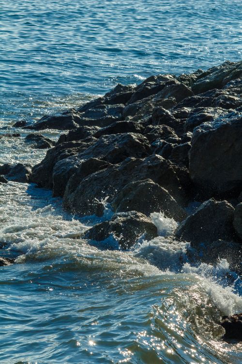 Free Waves crashing against a rocky coastline under clear skies for a serene, natural scene. Stock Photo