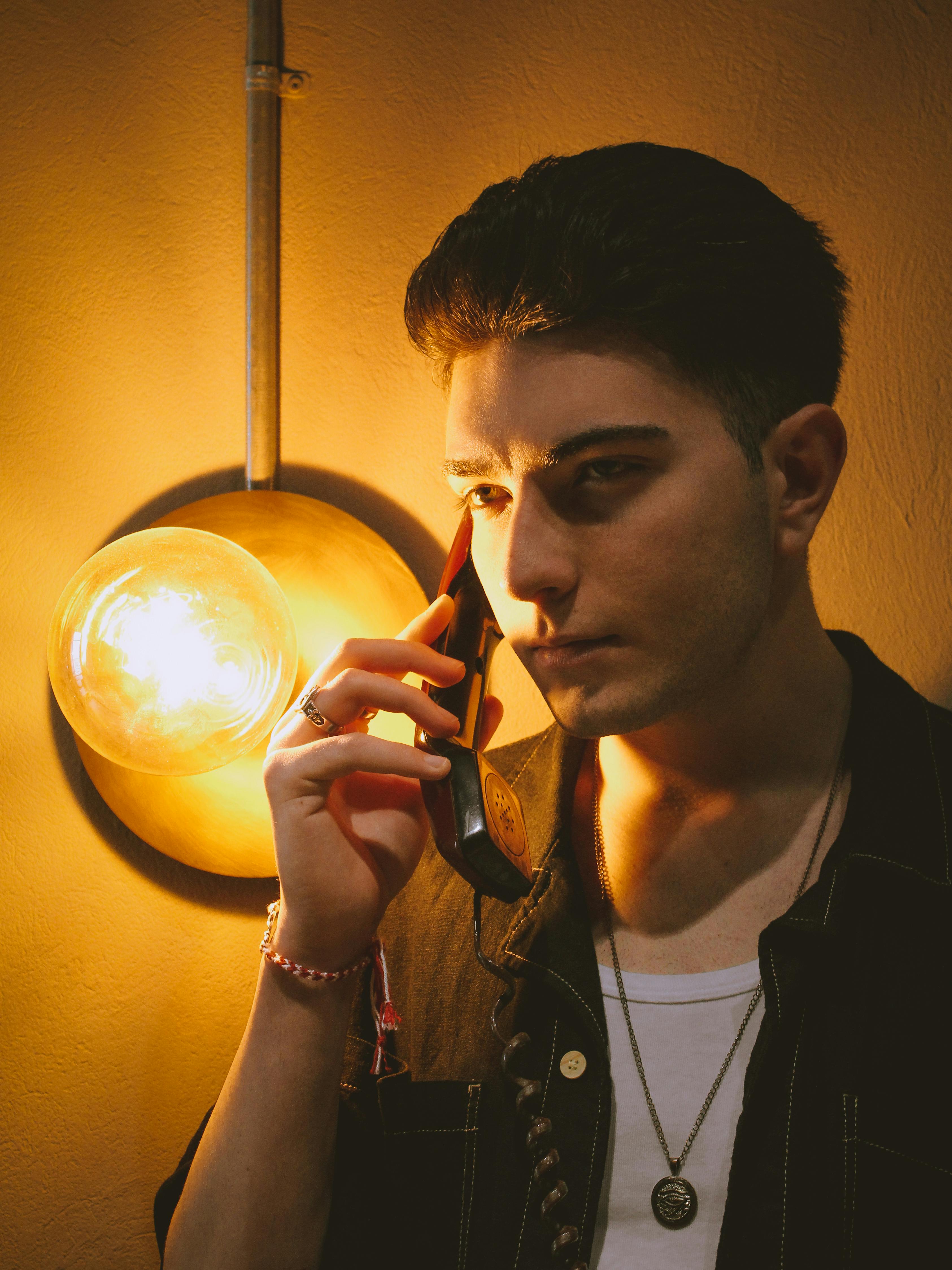 Young man in dim light talking on the phone, creating a moody atmosphere.