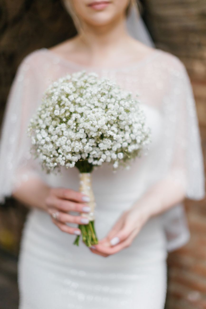 Bride in white dress holding a delicate baby's breath bouquet, captured in detail.