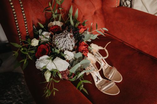 Free Luxurious bouquet with roses and protea atop a red velvet chair accompanied by elegant strappy heels. Stock Photo