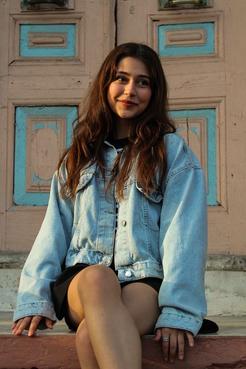 Free Young woman sitting on steps, wearing a denim jacket with a warm smile. Stock Photo