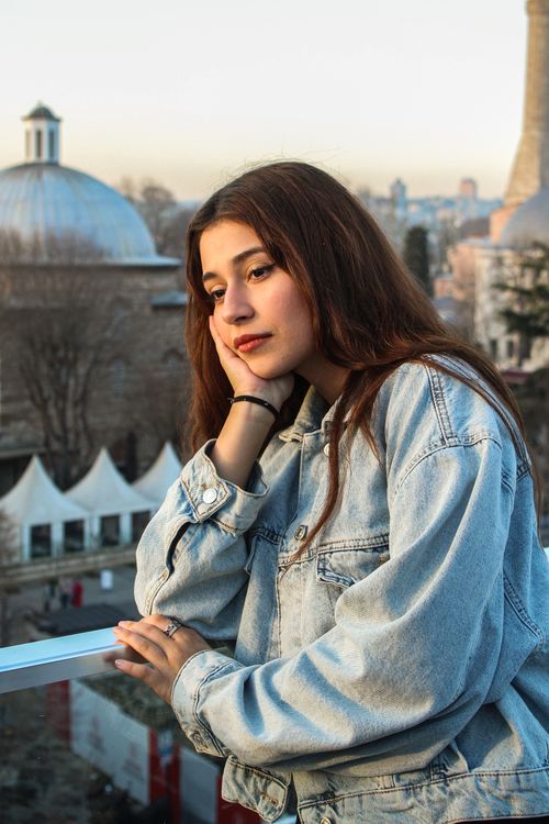 Free Pensive young woman in denim overlooking city skyline from a rooftop. Stock Photo