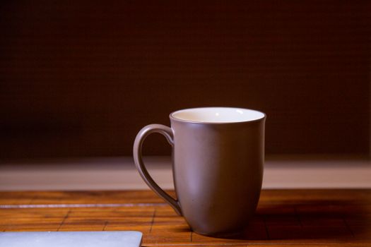 Simple brown ceramic mug on a wooden table with subdued lighting.