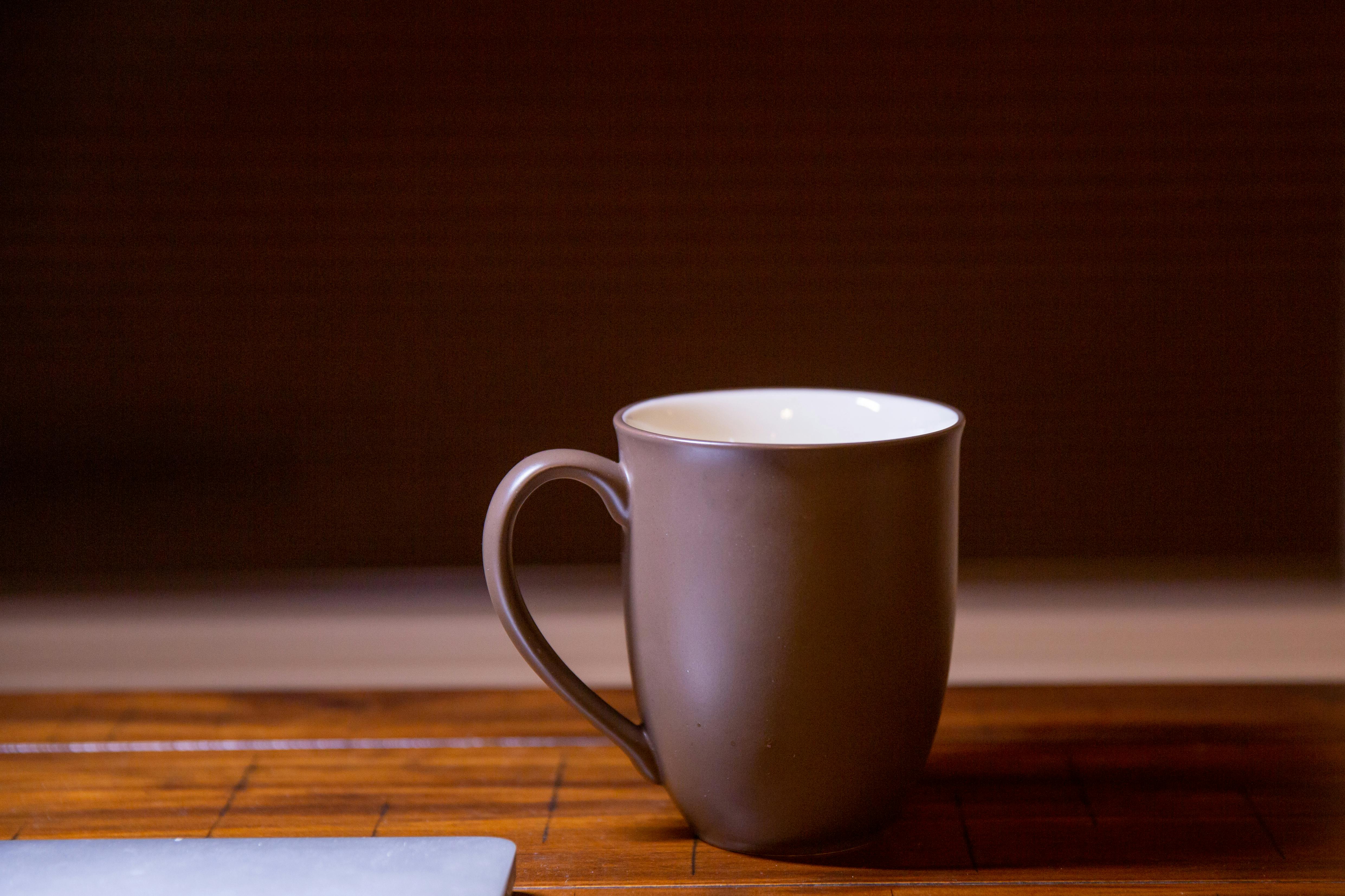 grátis Caneca simples de cerâmica marrom sobre uma mesa de madeira com iluminação suave. Foto profissional