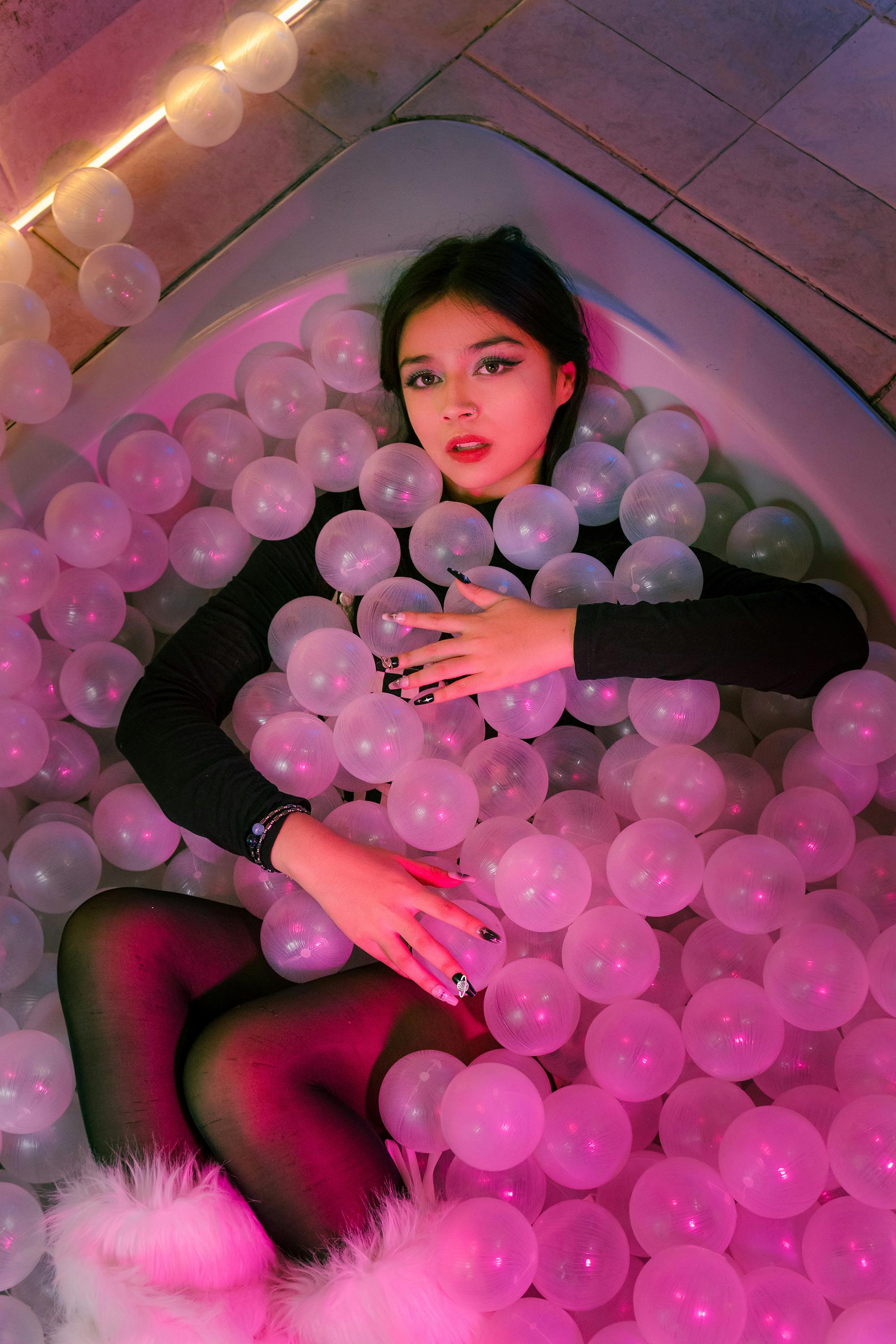 A young woman in a bathtub filled with pink balloons during a creative indoor photoshoot in Mexico City.
