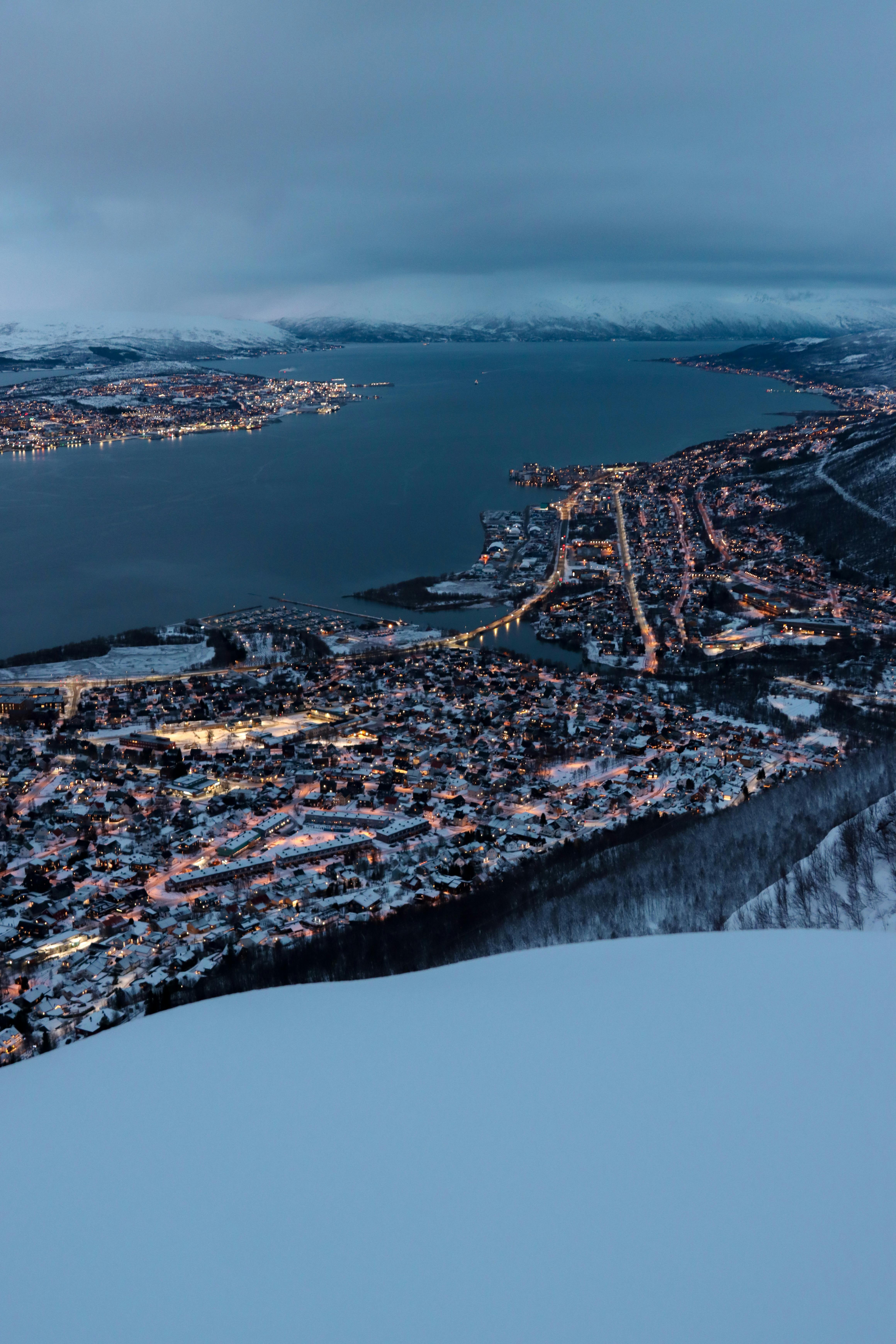 Captivating aerial view of Tromsø, Norway during winter twilight with city lights and snow.