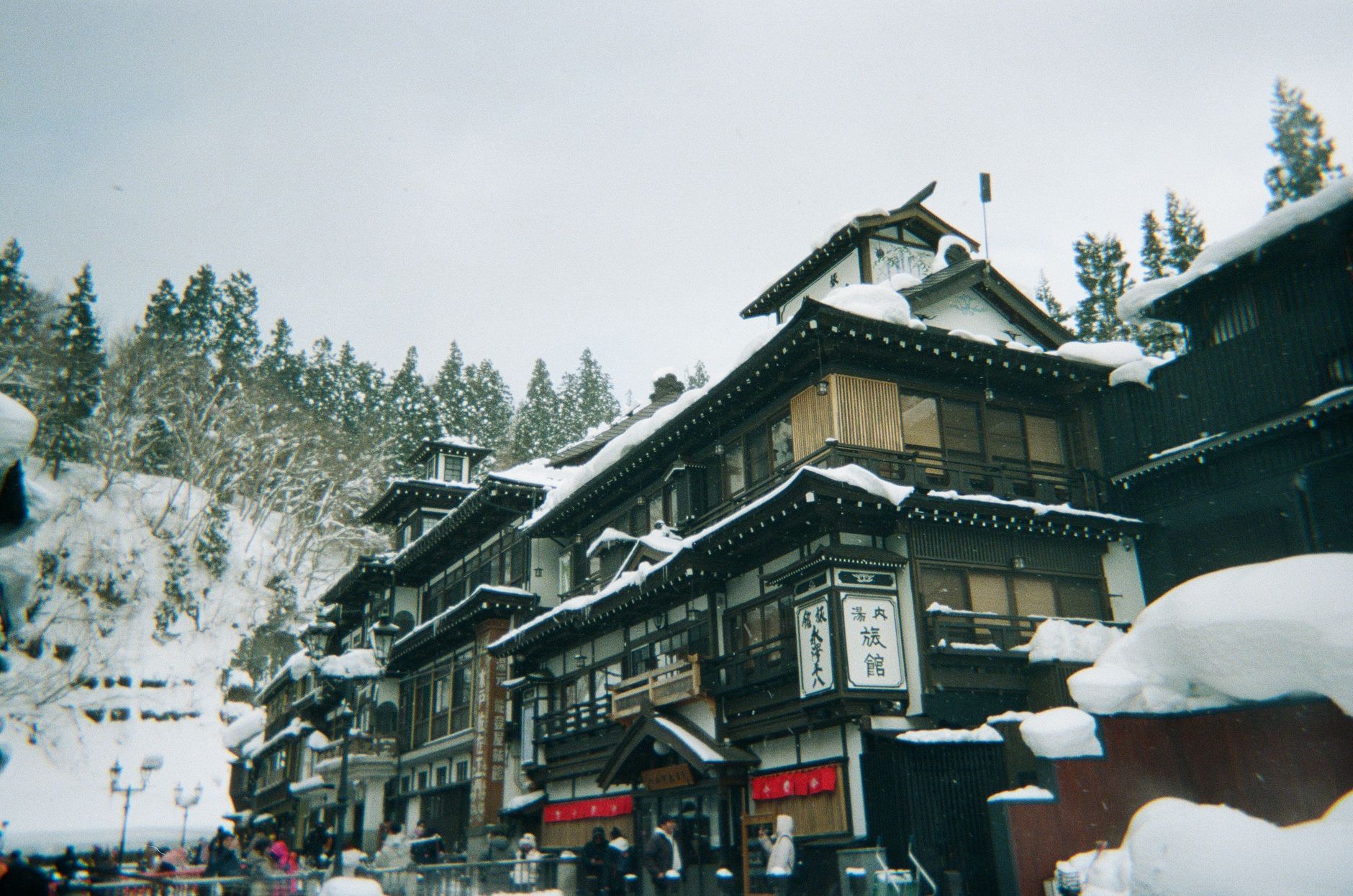 A picturesque view of traditional Japanese architecture in a snowy onsen town, set against a backdrop of snow-covered trees.