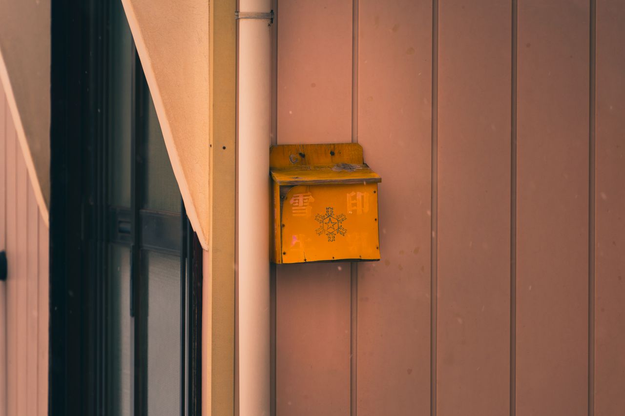 snow dusted yellow mailbox mounted on a pink wooden wall winter settin