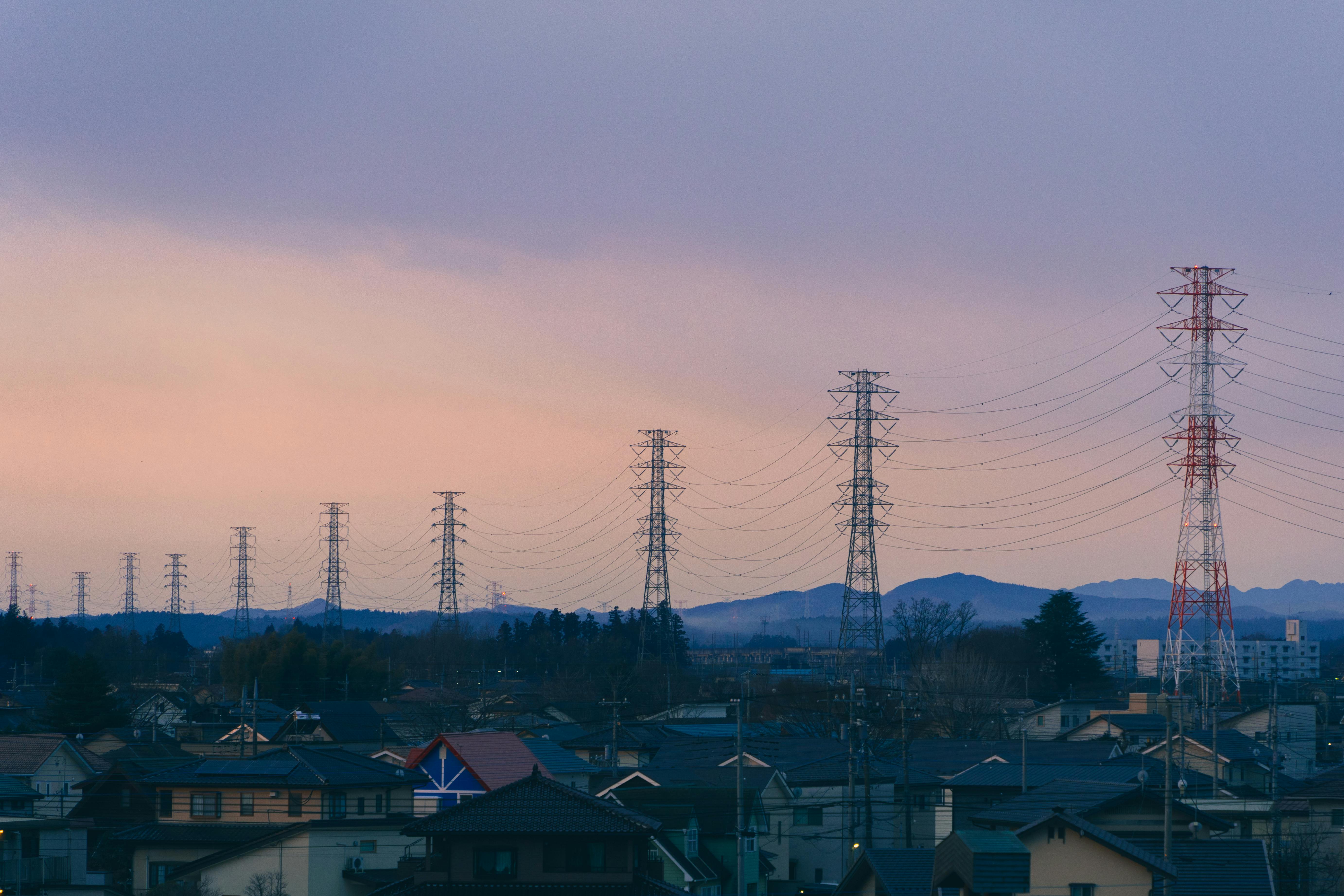 A suburban scene at dusk featuring rows of power lines and distant mountains under a colorful sky.