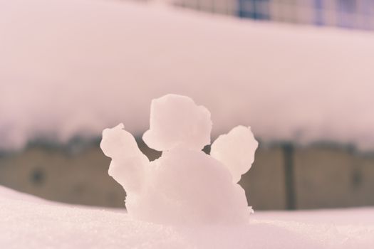 A small snow sculpture on a sunny winter day with soft pink hues.