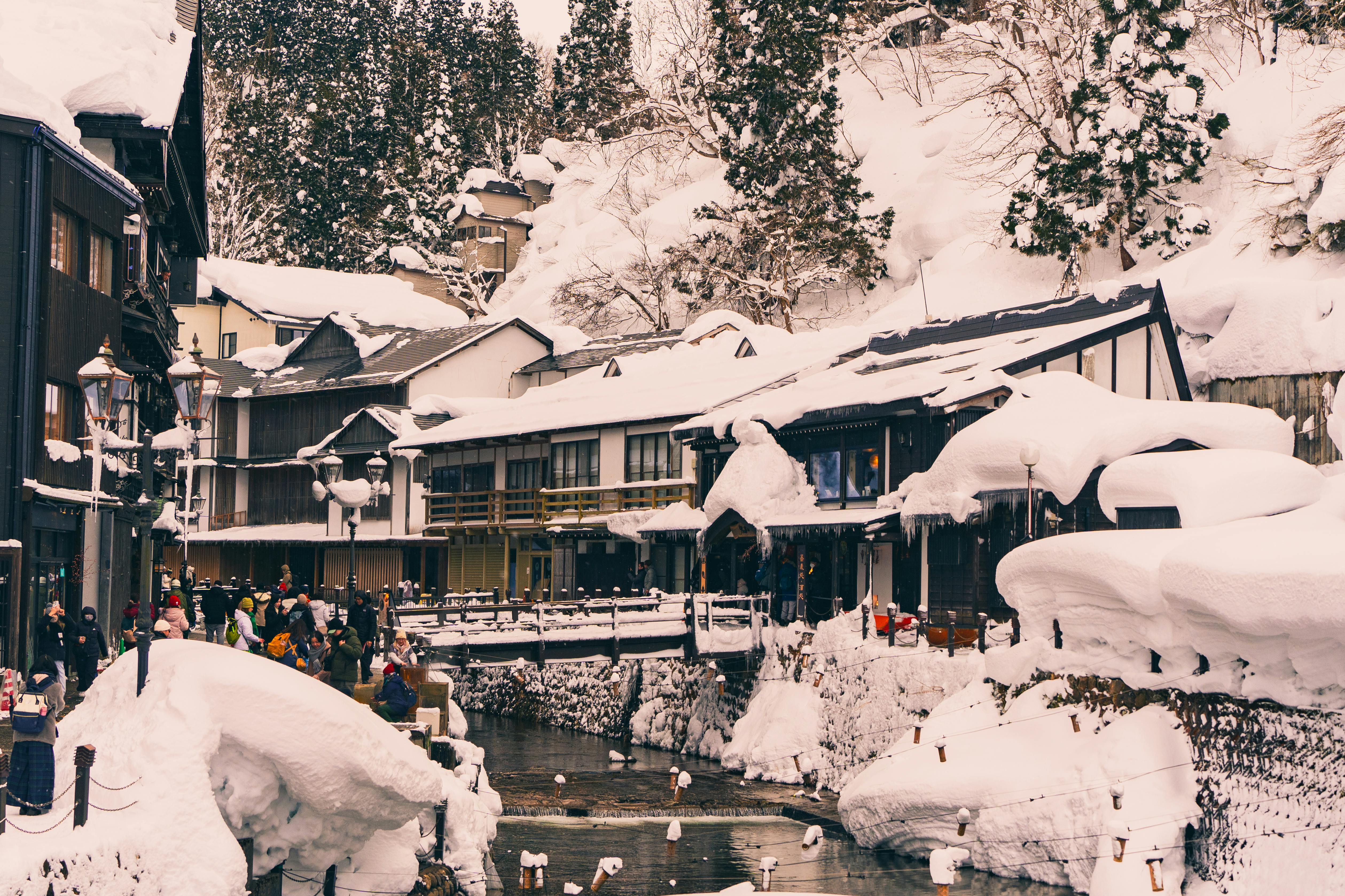 Charming snow-covered Japanese village with people enjoying winter activities by a river.