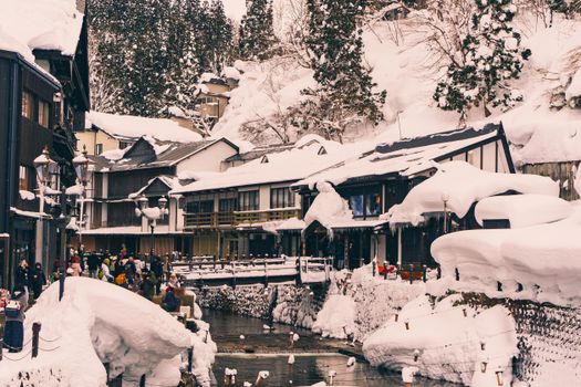 Charming snow-covered Japanese village with people enjoying winter activities by a river.
