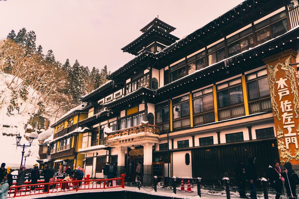 Multi-story wooden ryokan buildings and a red footbridge in snowy Ginzan Onsen