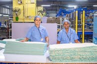 Two Indian female factory workers smiling in textile manufacturing facility.
