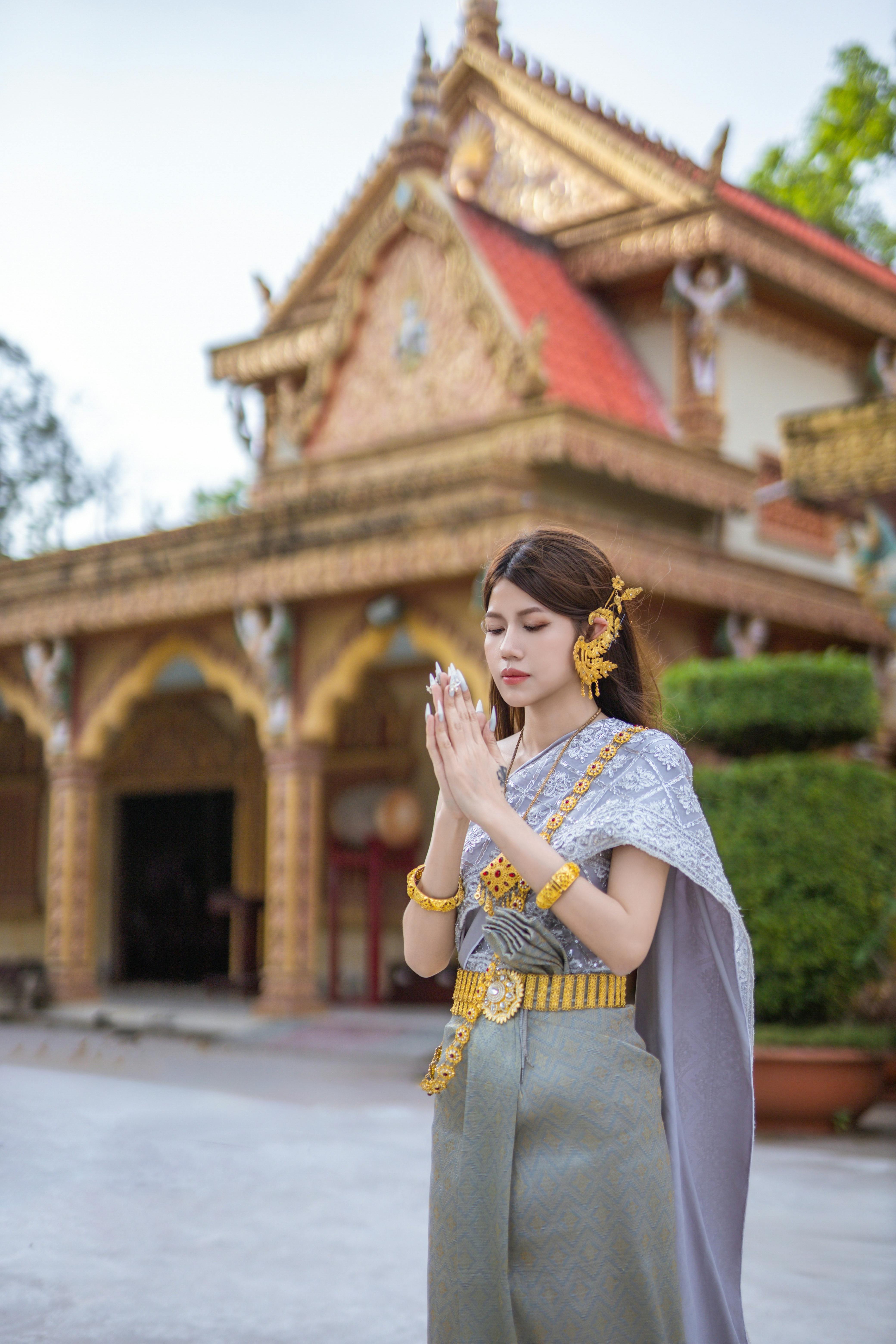 Elegant woman in traditional Thai dress praying at a temple, showcasing cultural beauty and heritage