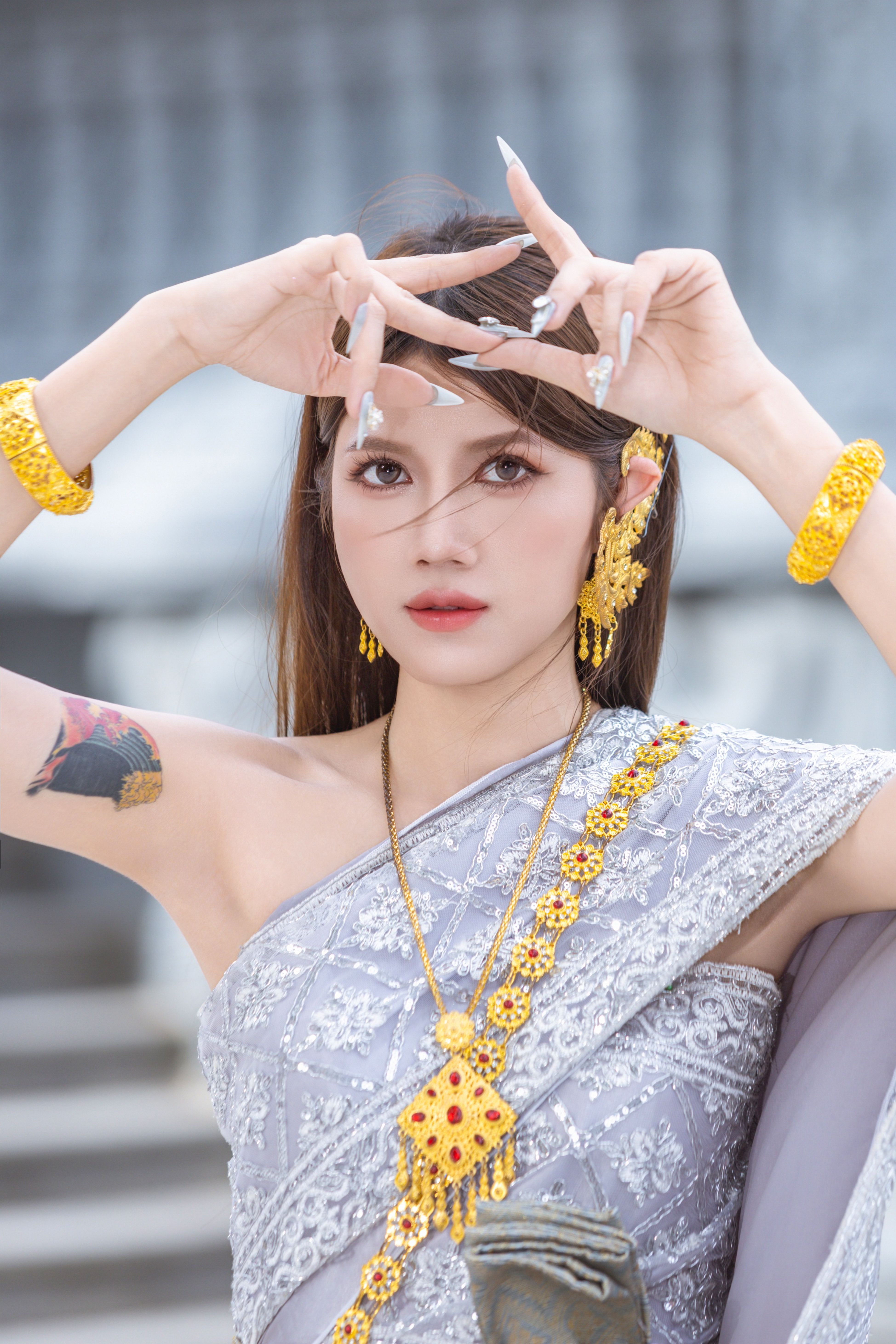 Woman posing in traditional Thai attire with gold jewelry and intricate patterns.