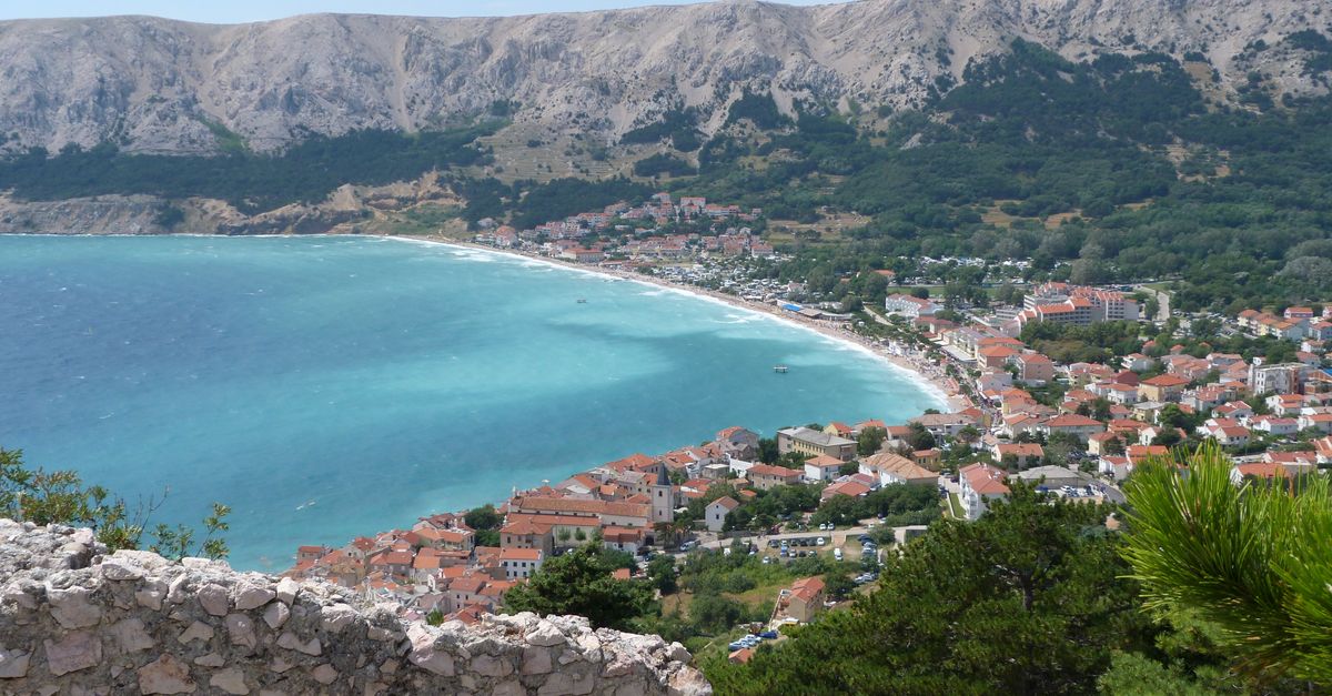 A stunning aerial view of Baška on Krk Island with turquoise waters and mountain backdrop.