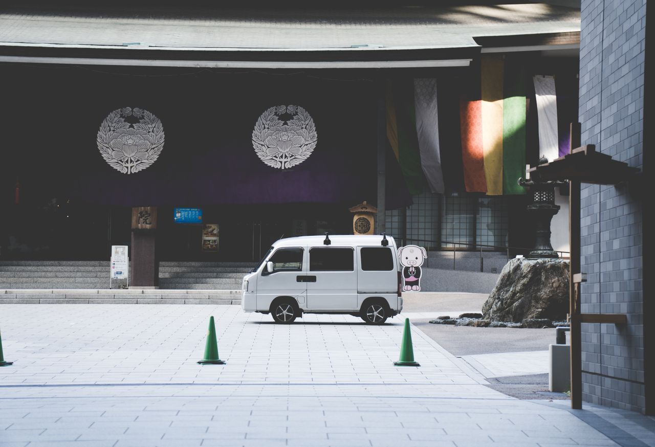 white kei van parked in front of an osaka shrine with colorful banners
