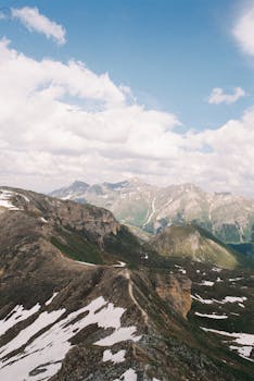Breathtaking aerial view of the Austrian Alps with snow patches and a bright sky.