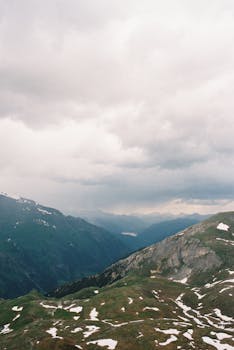 Stunning view of the Austrian Alps under a cloudy sky, showcasing rugged terrain and snow patches.