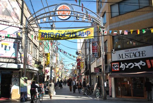 Bustling street scene in Japan filled with people, shops, and colorful banners under daylight.