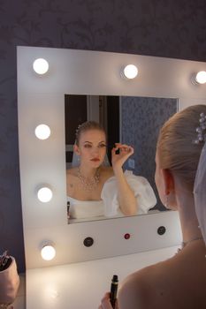 Beautiful bride applying makeup while sitting in front of a lighted vanity mirror.