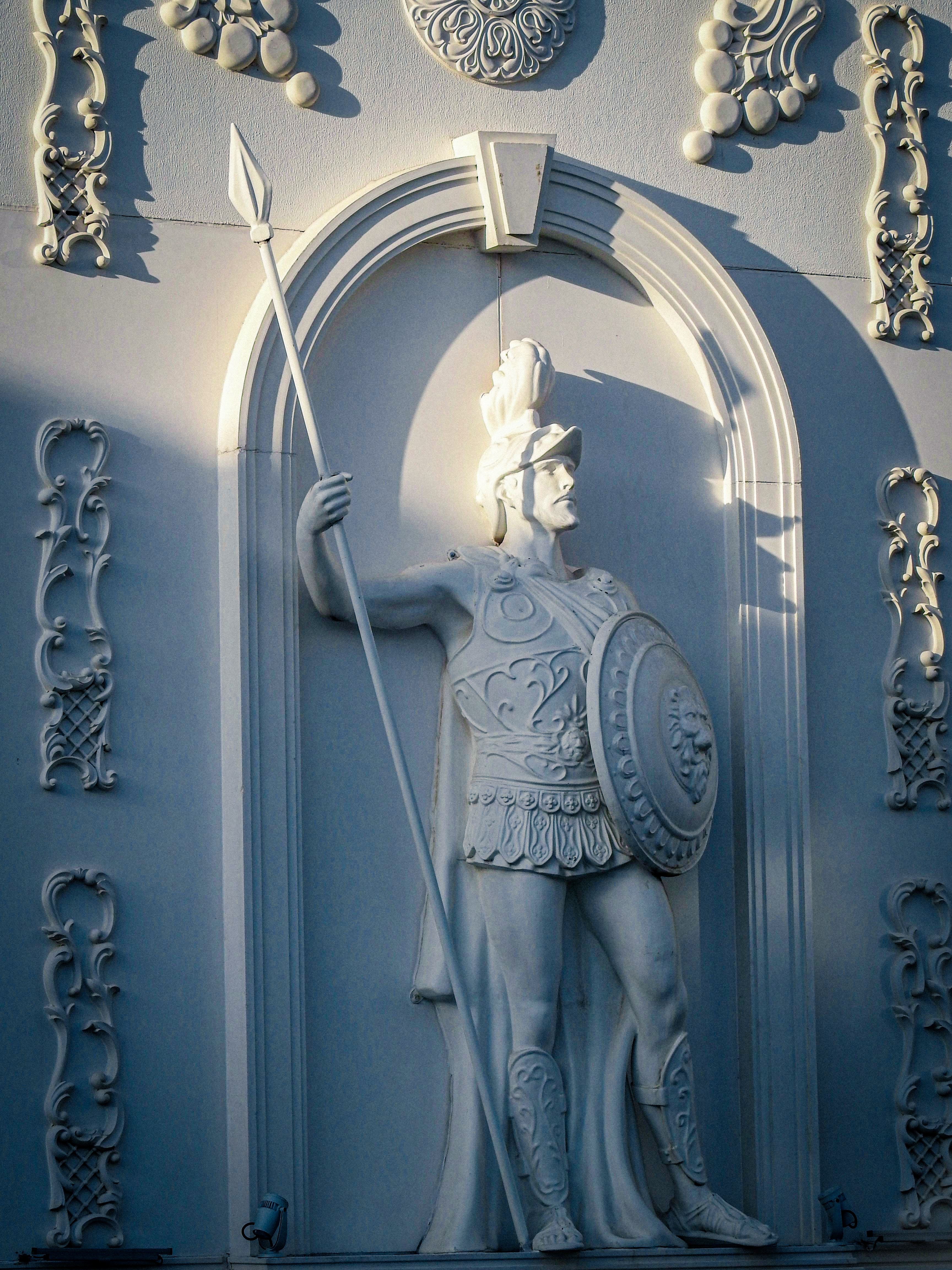 A detailed classical warrior statue adorned with spear and shield in intricate relief.