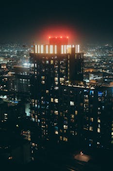 Dramatic aerial night view of a modern Los Angeles skyscraper glowing with city lights.