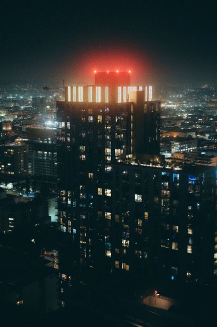 Dramatic aerial night view of a modern Los Angeles skyscraper glowing with city lights.